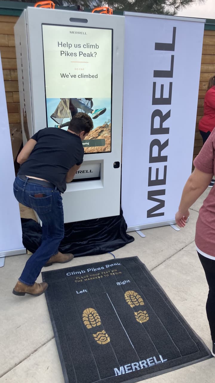 Attendee interacting with Merrell kiosk and custom Climb Pikes Peak foot pad