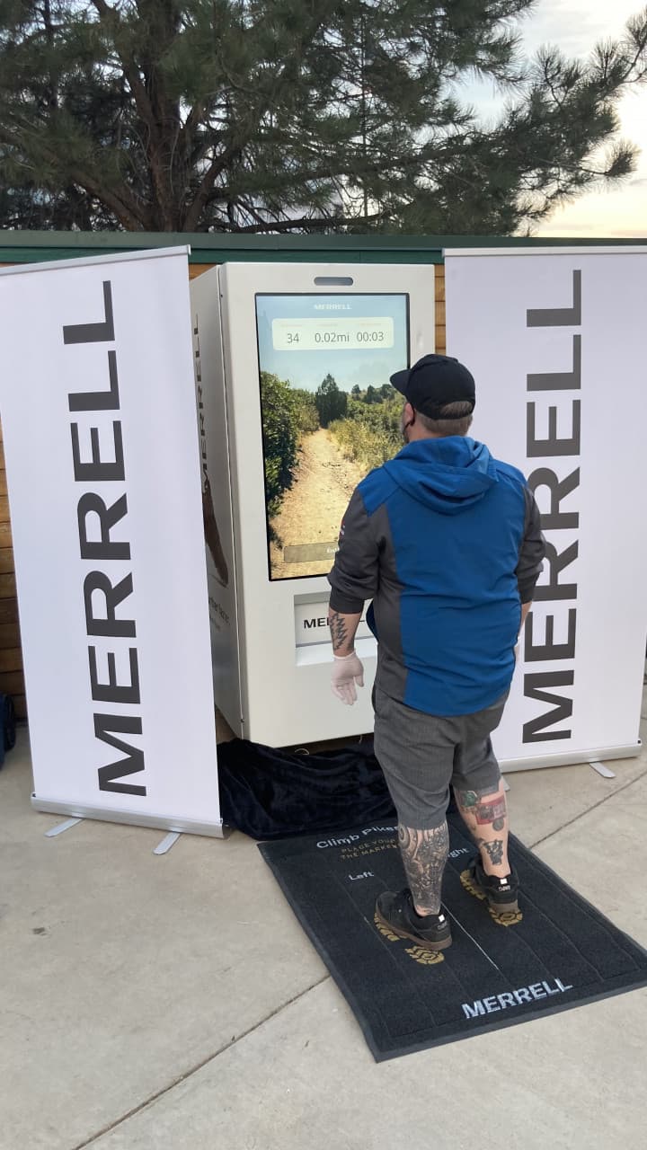 Attendee racing on Merrell speed challenge foot pad with trail gameplay on screen