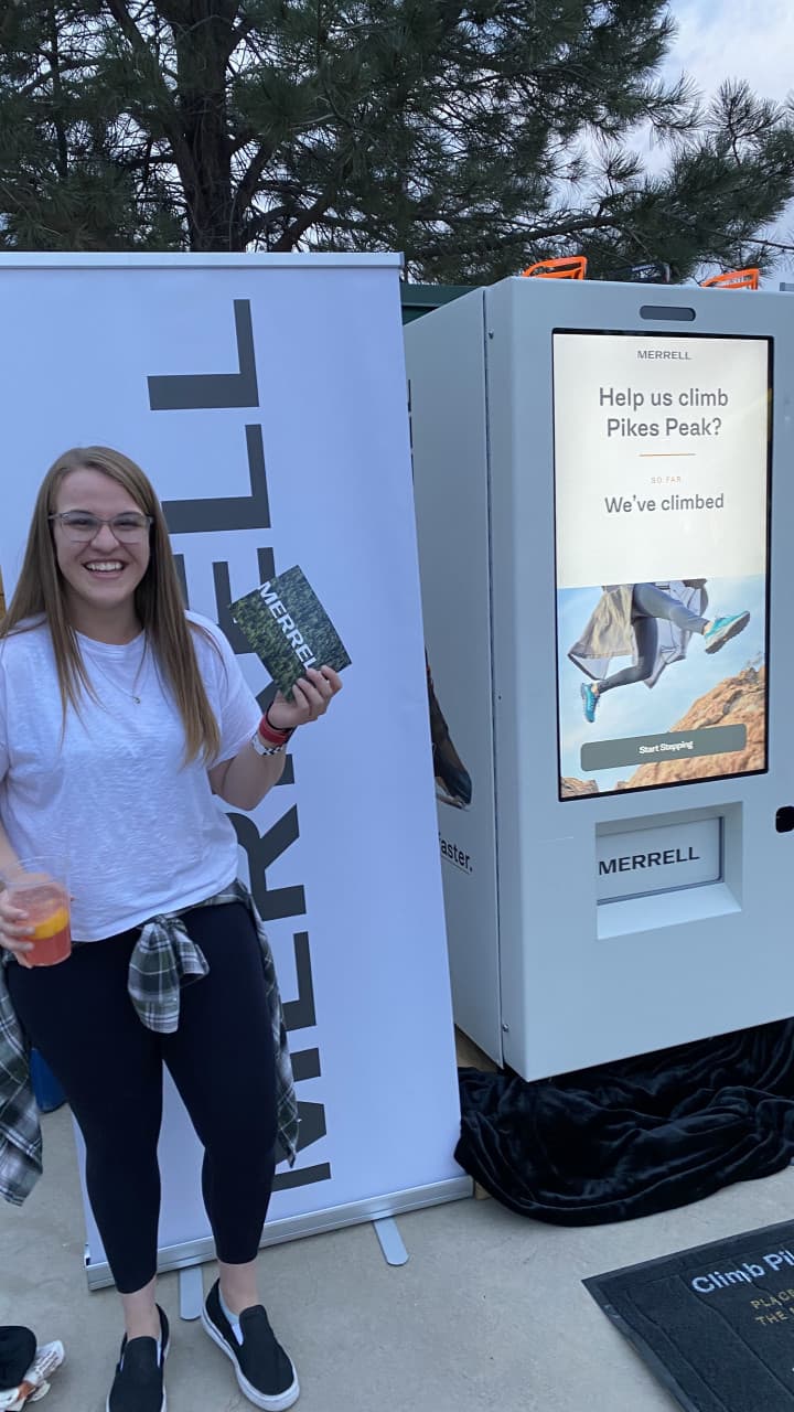 Attendee holding Merrell prize card next to Climb Pikes Peak kiosk activation